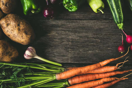 Vegetables on wood background, frame composition. Potatoes, carrots, garlic, peppers, zucchini and...