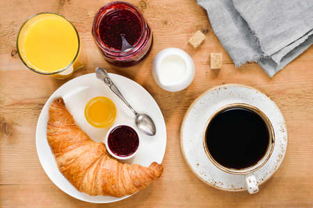 Croissant, cup of coffee, cream, orange juice, honey and jam on wooden table. Breakfast in cafe, hotel, continental breakfast or coffee break conceptの写真素材