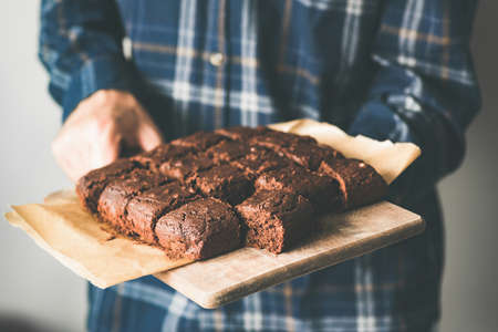 Vegan chocolate brownies on baking sheet. Young person holding plate with freshly baked vegan marijuana chocolate cakesの写真素材