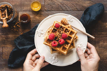 Eating waffles for breakfast. Person holding plate of belgian waffles with raspberries, granola and...