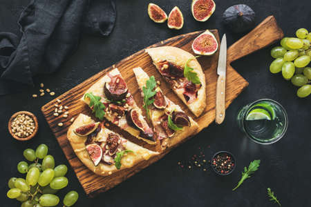 Flatbread with figs, prosciutto, grapes, arugula on wooden serving board. Top view, toned image. Sliced pizzaの写真素材