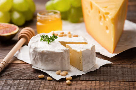 Cheese plate with brie, camembert, maasdam cheese and fruits green grapes, figs, pine nuts and thyme. Closeup view. Gourmet appetizer plateの写真素材