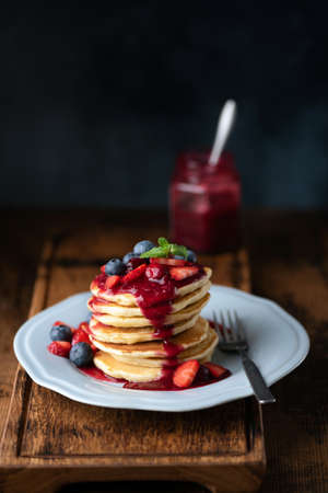 Pancakes with berries and strawberry sauce on wooden serving board, darkの写真素材
