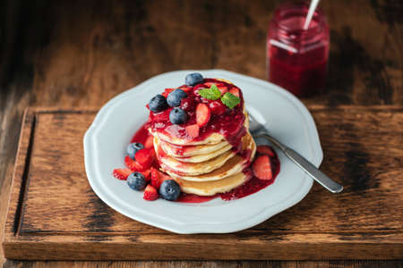 Pancakes with berry sauce and fresh berries on wooden serving board. Tasty breakfast or dessert