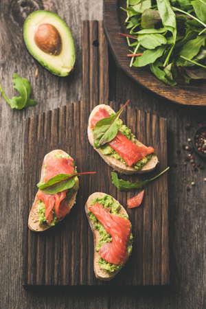 Salmon toast with avocado on wooden cutting board, top view.