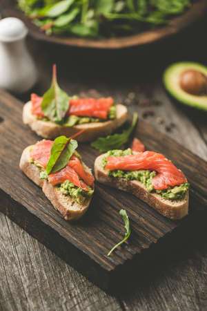 Healthy Open Sandwiches With Avocado and Salmon On Wooden Cutting Board. Selective focus, Toned imageの写真素材