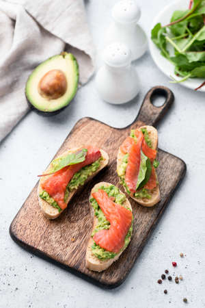 Tasty sandwiches with avocado and salmon on wooden cutting board