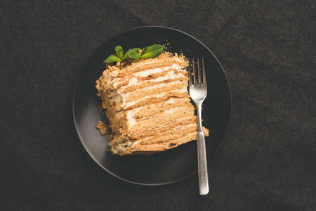 Russian honey cake Medovik on black plate, top view, toned image