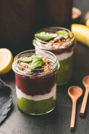 Layered acai avocado smoothie in jar topped with granola and spinach leaf, healthy breakfast or...