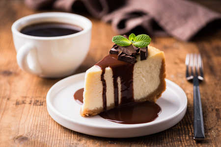 Cheesecake with chocolate sauce and cup of black coffee on a wooden table. Tasty snack or coffee time with slice of cakeの写真素材