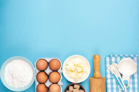 Ingredients for baking or cooking on blue background. Eggs, butter, flour, measuring spoons and...