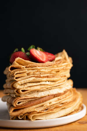 Stack of crepes or blini on wooden table, black background. Copy space for text. Maslenitsa food