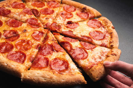 Taking slice of pepperoni pizza. Tasty pepperoni pizza on blackの写真素材