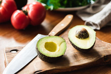 Halved avocado on wooden cutting board. Healthy vegetarian or vegan cooking process