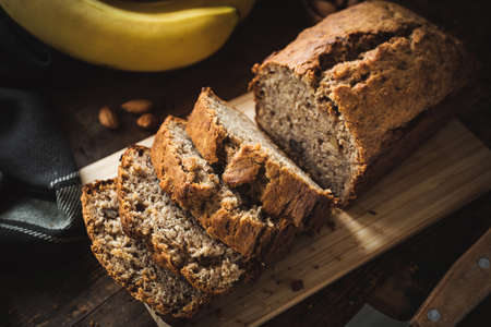 Homemade banana bread or cake loaf sliced on wood. Soft morning light, dark moody food photography....