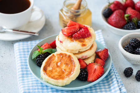 Cottage cheese pancakes syrniki with strawberry, blackberry and honey on blue plate. Tasty healthy...