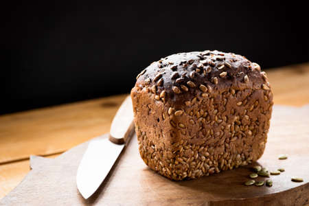 Loaf of wholemeal rye bread with sunflower seeds on wooden cutting board.