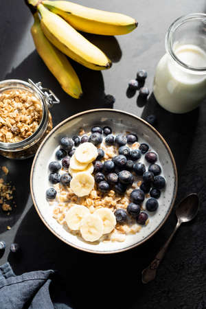 Breakfast cereal oat granola with banana and blueberry in bowl on black concreteの写真素材
