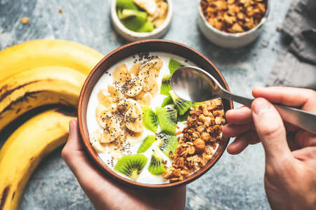 Eating healthy vegetarian breakfast smoothie bowl with granola, banana, kiwi and chia seedsの写真素材
