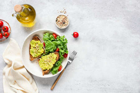 Avocado toast served with fresh green salad of kale, olive oil and tomatoes. Vegan, vegetarian food.の写真素材