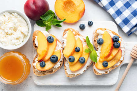 Peach bruschetta with ricotta cheese and blueberries on white wooden serving board.の写真素材