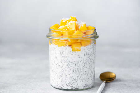 Chia seed pudding with mango and coconut in glass jar on bright grey concreteの写真素材