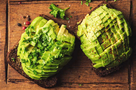 Rye toast with avocado, parsley and spices on wooden cutting board, table top viewの写真素材