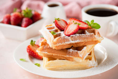 Belgian waffles with strawberry and powdered sugar on white plate, pink backgroundの写真素材