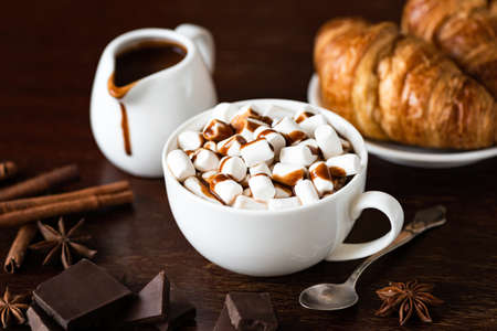 Hot chocolate with marshmallow in white cup on brown wooden table. Hot chocolate with spices winter...