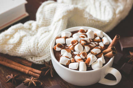 Cup of hot chocolate with marshmallows and cinnamon on wooden table, closeup view. Winter comfort...