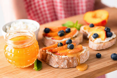 Sweet bruschetta with ricotta, peach and honey on a wooden tray. Healthy snack, breakfast, summer...