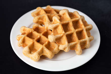 Homemade belgian waffles on plate, isolated on black background. Breakfast food sweet golden crunchy...