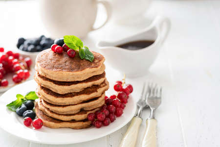 Whole wheat pancakes with berries on white table, healthy breakfast stack of pancakes. Copy space on white backgroundの写真素材