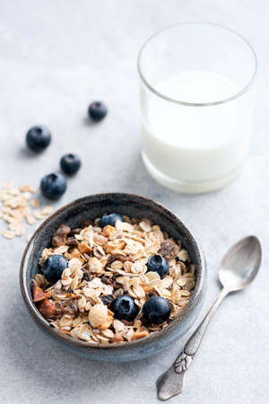 Muesli with blueberries and glass of milk on grey concrete table.