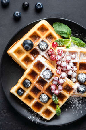 Square belgian waffles with berries and confectionery sugar on black plate, top viewの写真素材