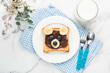 Food art bear toast for kids with chocolate nut spread, fruits and glass of milk.の写真素材
