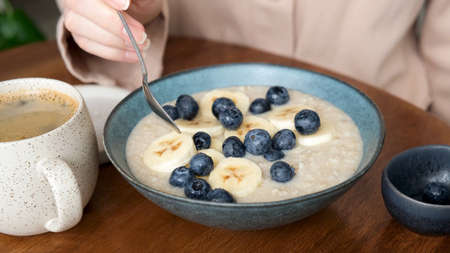 Healthy breakfast bowl of oatmeal porridge with blueberries and banana slices. Woman eating healthy...