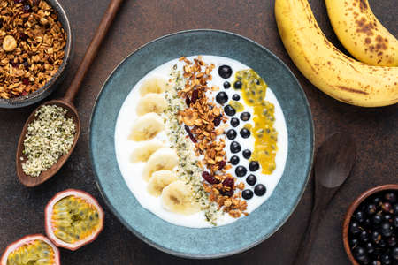 Yogurt bowl with granola and tropical fruits on brown background. Top view. Healthy vegetarian...