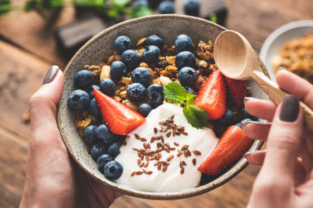 Bowl of granola with fruits and greek yogurt in female hands. Fitness food menu, dieting, clean...
