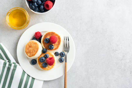 Cottage cheese fritters with berries and honey on plate. Russian Ukrainian cuisine sweet food for...