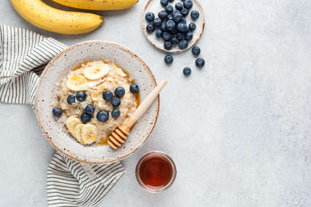 Breakfast oatmeal bowl with blueberries, banana, coconut and honey on grey concrete table background, top view with copy space for text, designの写真素材