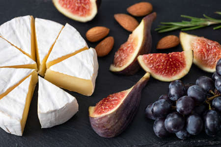 Camembert cheese with figs and grapes on black slate background. Appetizer cheese platterの写真素材