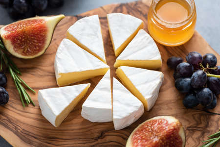 Camembert or brie cheese with figs, grapes and honey on wooden serving board. Cheese plateの写真素材