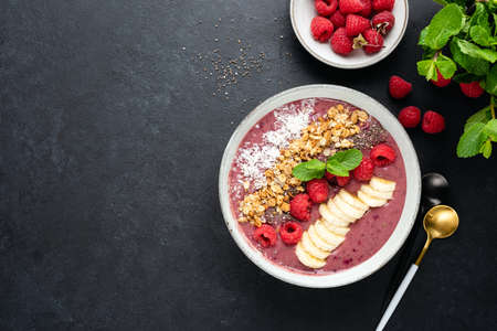Raspberry smoothie bowl with superfood toppings on black background, top view, copy space. Vegan vegetarian detox smoothie bowlの写真素材