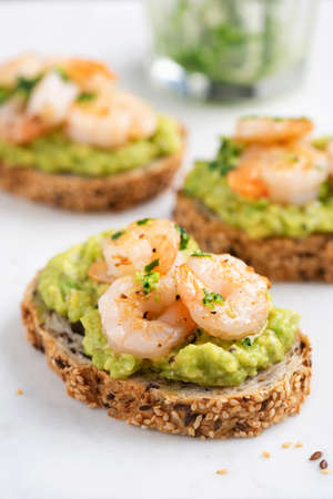Bruschetta with avocado cream and shrimps on white marble background, closeup view. Appetizer or snack avocado toasts with prawnの写真素材
