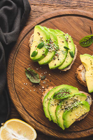 Healthy vegan avocado toast with hemp seeds on wooden cutting board, top viewの写真素材