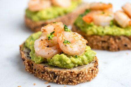 Healthy appetizer or snack avocado shrimp bruschetta with whole grain bread on white marble, closeup view. Fried shrimp and mashed avocado on a toasted breadの写真素材