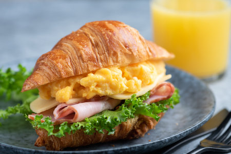Croissant sandwich with ham, cheese, scrambled eggs and lettuce salad. Closeup view. Tasty healthy breakfast sandwichの写真素材