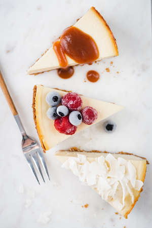 Three slices of cheesecake with various toppings. Caramel sauce, frozen berry and coconut cheesecakeの写真素材