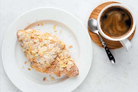Coffee cup and almond croissant on white marble table. Coffee break, morning breakfast foodの写真素材